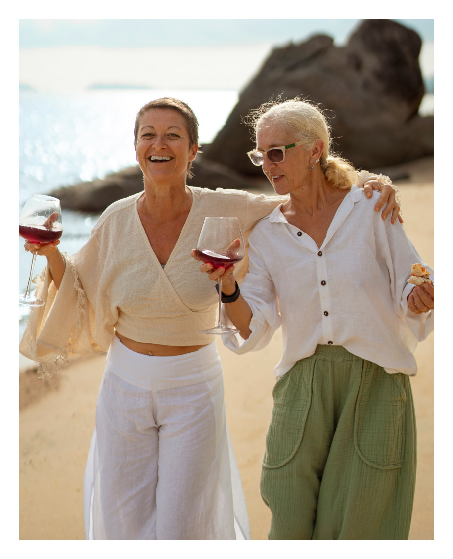 Two women enjoying the wine with beach on the background